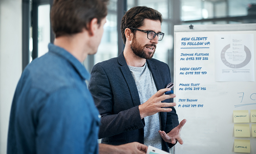 A man giving a speech next to a whiteboard with new clients listed