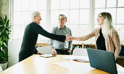 People shaking hands across a table with man in the middle looking to left