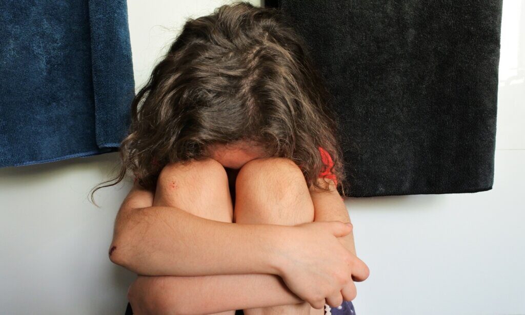 Sad young girl (female age 6-7) covering her face crying in bathroom.